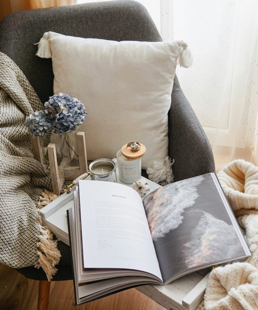 Cozy armchair corner with a knit throw, white pillow, candle, and an open book